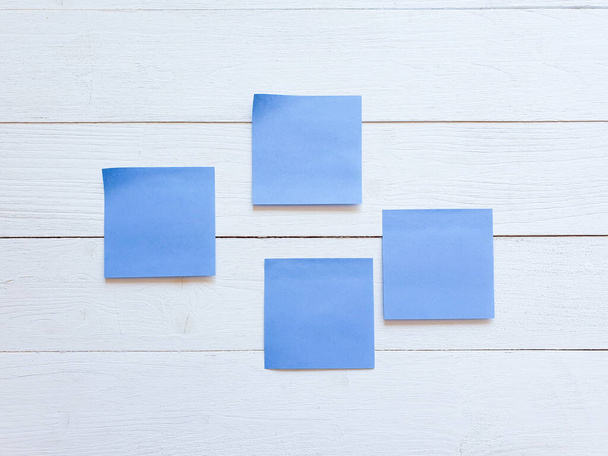Vier blaue Papieraufkleber auf weißem Holzbrett. - Foto, Bild