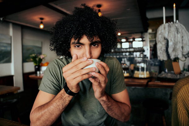 Handsome young man with curly hair sipping hot coffee relaxing in cafe - Foto, imagen