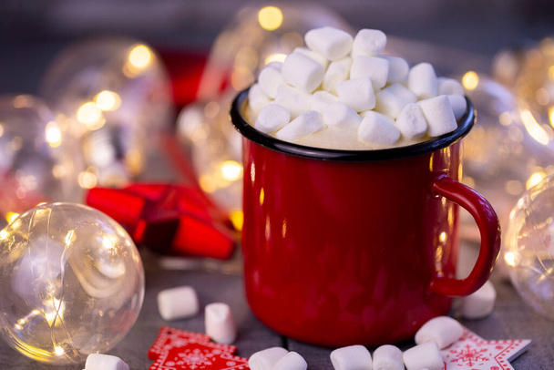 Кубок красный кофе освещается рождественской гирляндой с рождественским декором крупным планом - Фото, изображение