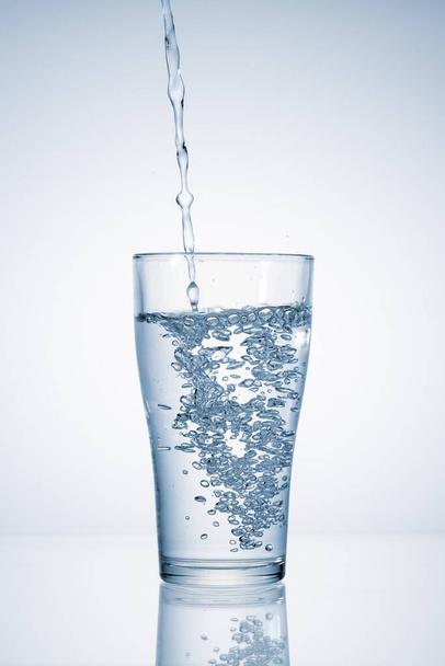 Zoet mineraalwater gieten in glas op blauwe achtergrond met kopieerruimte - Foto, afbeelding