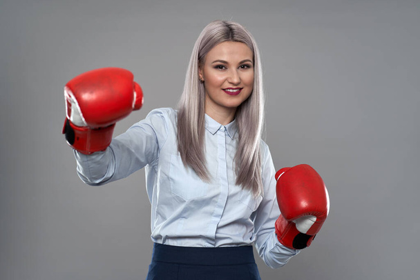Young combative businesswoman with boxing gloves on gray background - Foto, Imagen