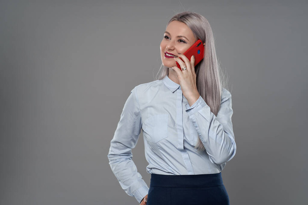 Young businesswoman speaking on her mobile phone, gray background - Foto, afbeelding