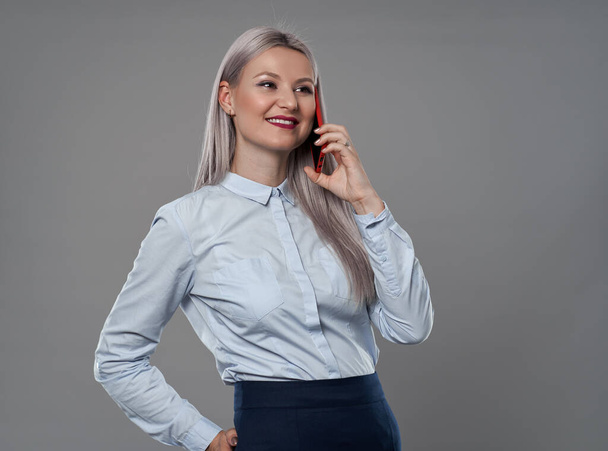Young businesswoman speaking on her mobile phone, gray background - Foto, immagini
