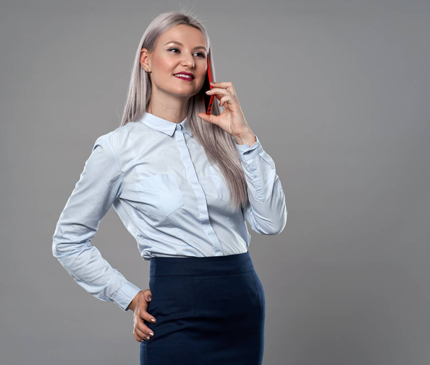 Jonge zakenvrouw spreekt op haar mobiele telefoon, grijze achtergrond - Foto, afbeelding