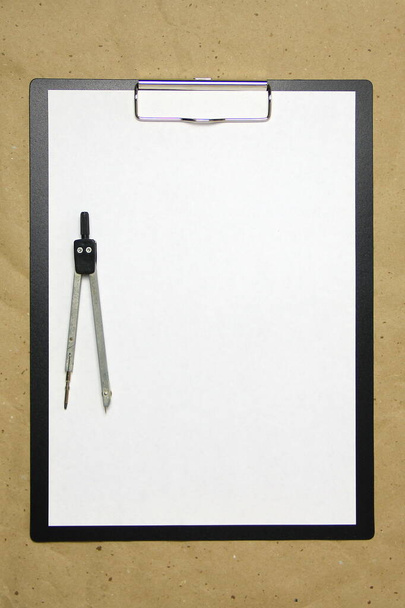 A tablet with a white sheet of A4 format with divivder on a beige craft paper. Concept of accurate measurements, study and construction. Stock photo with empty place for your text and design. - Fotó, kép