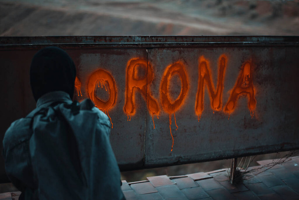Κρυμμένος άνθρωπος γράφει Corona σε ένα εγκαταλελειμμένο τοίχο με σπρέι - Φωτογραφία, εικόνα