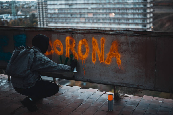 Νεαρός γράφει Corona Virus σε μια στέγη εγκαταλελειμμένου κτιρίου με σπρέι μπογιάς - Φωτογραφία, εικόνα