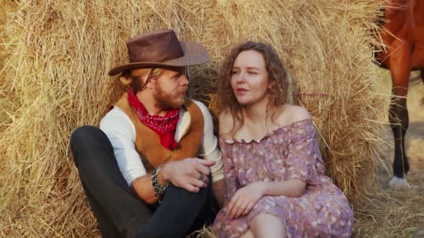 Auf dem Hof sitzt ein junges Paar auf Heu. Glücklich lächelnder Cowboy und Frau verbringen Zeit miteinander - Filmmaterial, Video