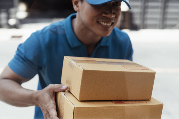 Sonriente alegre tailandés repartidor en azul de trabajo custume llevar cajas de cartón. - Foto, Imagen
