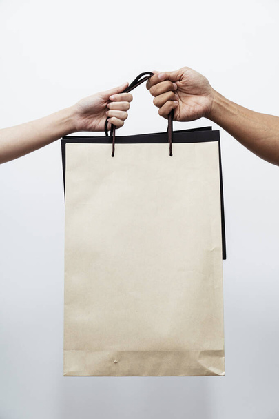 Two people hands holding shopping paper bags together isolated on white background. - Фото, изображение