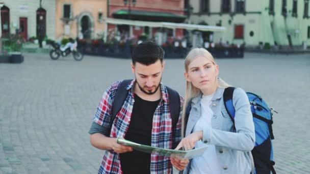 Young couple of tourists with map looking for new historical place in city center - Footage, Video