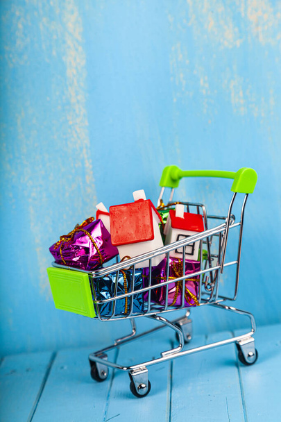 Business still life. Homes and gift boxes in a shopping cart. Buying or selling real estate. - Foto, Imagen