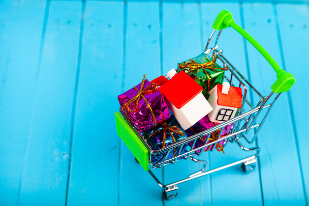 Business still life. Homes and gift boxes in a shopping cart. Buying or selling real estate. - Foto, imagen