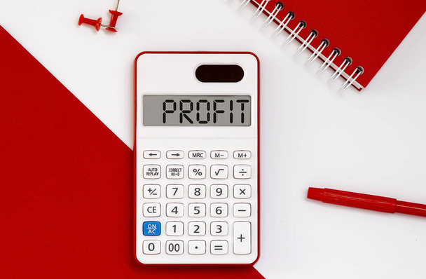 calculadora con la palabra PROFIT en pantalla con bloc de notas rojo y herramientas de oficina - Foto, imagen