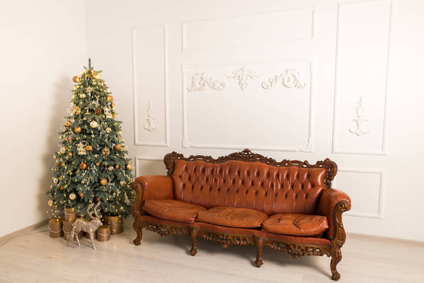 Vue latérale du studio intérieur de lumière de Noël. Chambre intérieure avec arbre festif et canapé marron - Photo, image