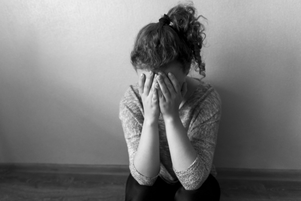 Tyttö istuu lattialla ja itkee peittäen kasvonsa käsillään, mustavalkoinen kuva - Valokuva, kuva