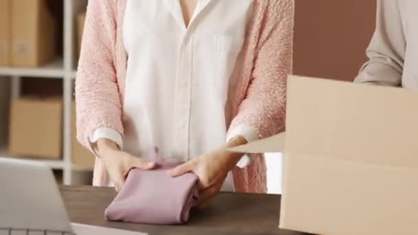 Mid-sectie tracking shot van onherkenbare vrouwen vouwen en zetten kleding in kartonnen doos tijdens het verpakken van bestellingen voor online winkel - Video