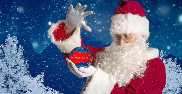 Święty Mikołaj trzyma szklaną kulę z napisem zimowa wyprzedaż w ręku - Zdjęcie, obraz