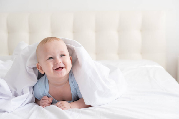 面白い赤ちゃんが笑顔で家の白い寝具に横になって.  - 写真・画像