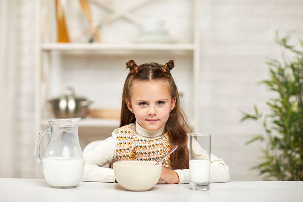 little girl eating breakfast: cereal with the milk in the kitchen. - Фото, зображення