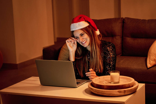 Sad young woman, dressed in a Santa Claus hat making a video call to her family to celebrate Christmas. Concept of loneliness, separated family, social distance and Christmas. - Photo, Image