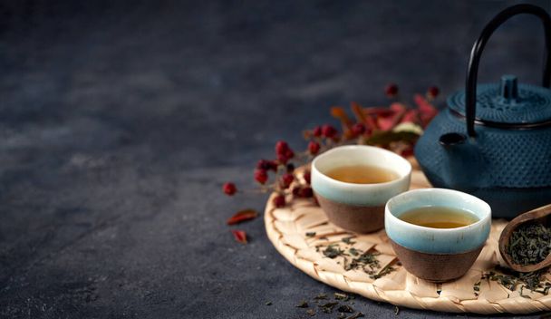 Asiatische Lebensmittel Hintergrund Banner mit grünem Tee, Tassen und Teekanne mit Blättern und Kopierplatz für Text auf dunklem Hintergrund. - Foto, Bild