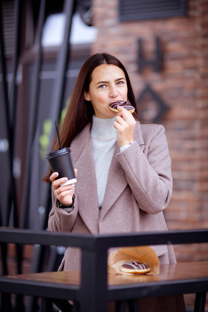 długowłosa brunetka jedząca pączki na ganku kawiarni - Zdjęcie, obraz