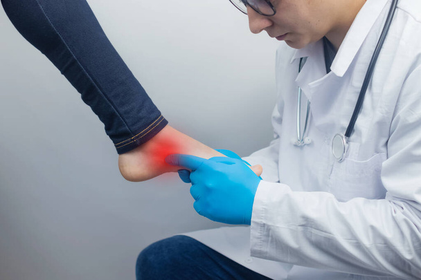 An orthopedic surgeon examines a woman's leg. Foot pain, tendon sprains, inflammation, flat feet, bursitis, fasciitis. Foot disease treatment concept. The doctor examines - Photo, Image