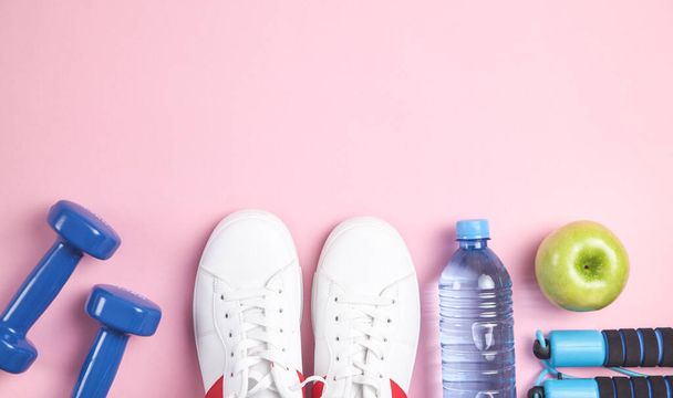 Fitnessgeräte. Hanteln, Apfel, Turnschuhe, Wasserflasche auf rosa Hintergrund. - Foto, Bild
