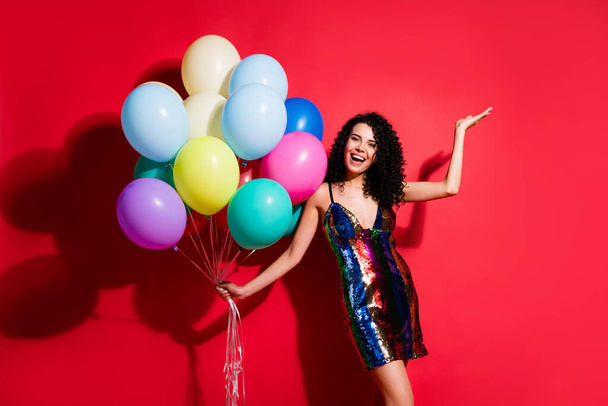Full length photo of gorgeous girl hold many balloons raise arm palm wear glossy short dress isolated bright red color background - Φωτογραφία, εικόνα