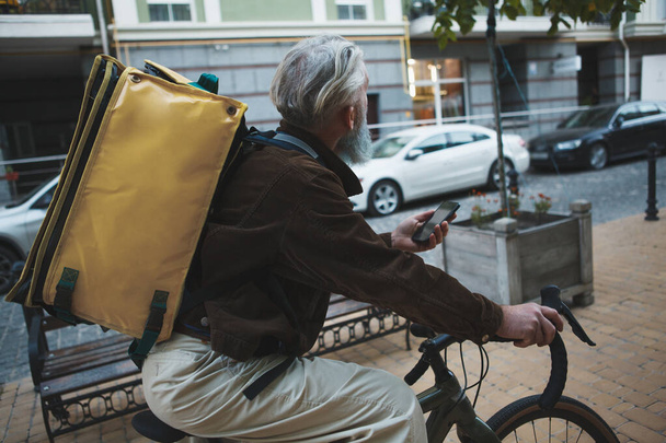 Vue arrière d'un livreur senior à vélo, portant un sac à dos de livraison - Photo, image