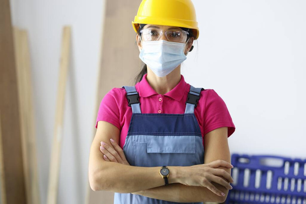 Woman in protective helmet wearing medical mask on face standing at construction site - Foto, Imagen