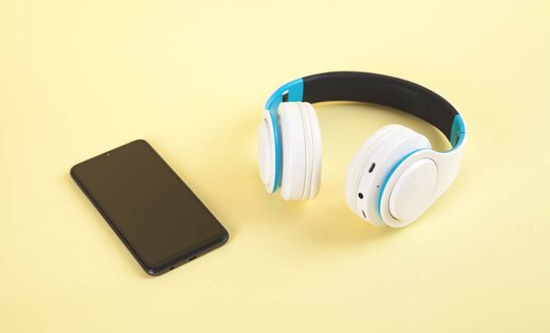 Bílá bezdrátová sluchátka a smartphone na žlutém pozadí. - Fotografie, Obrázek