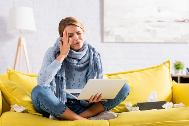 Ill woman suffering from headache while holding laptop on couch  - Fotografie, Obrázek