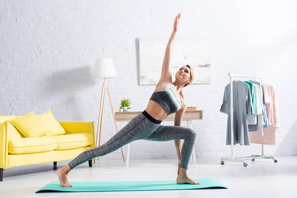 Bionda sportiva in piedi in yoga asana sul tappeto fitness  - Foto, immagini