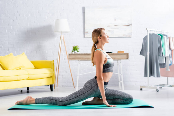 Side view of blonde sportswoman practicing yoga with closed eyes on fitness mat  - Fotografie, Obrázek