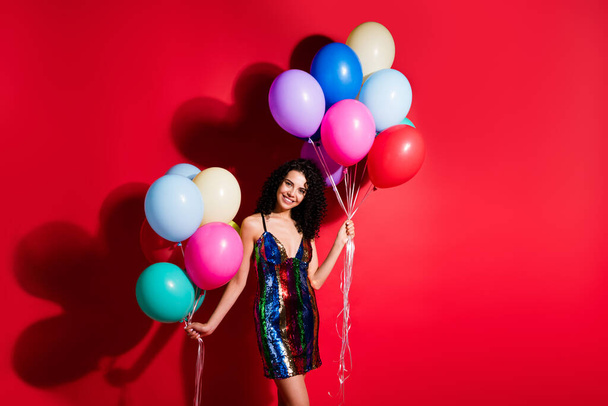 Photo of charming girl hold many balloons shiny beaming smile wear glossy short dress isolated vibrant red color background - Foto, imagen