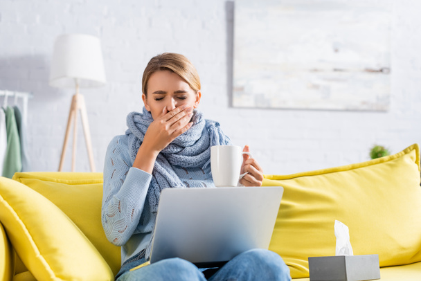 Sick freelancer coughing while holding cup near laptop and napkins  - Foto, afbeelding