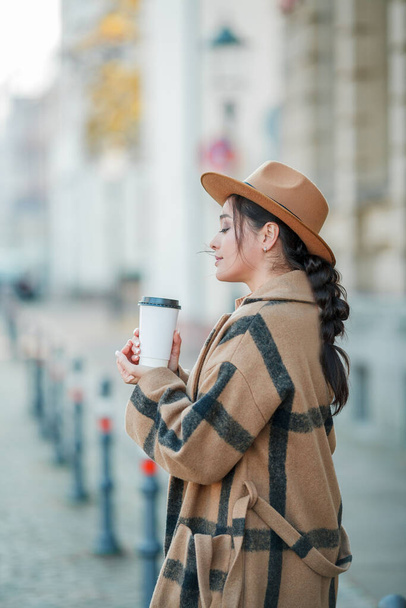 Nahaufnahme schöne junge Frau mit Hut und Kaffee Spaziergänge in einer europäischen Stadt - Foto, Bild