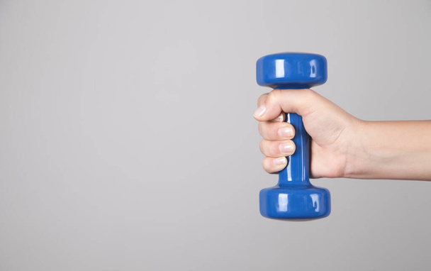 Girl hand holding dumbbell in gray background. - Photo, Image