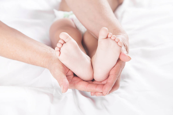 Babcia pokazując nogi małego dziecka na łóżku. - Zdjęcie, obraz