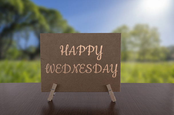 Happy Wednesday card on the table with sunny green forest background. - Photo, Image