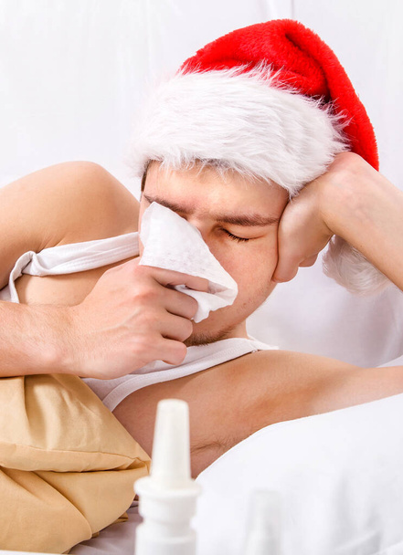 Sick Man in Santa Hat with a Handkerchief in the Bed closeup - Fotó, kép
