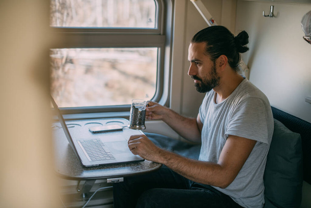 電車の中でノートパソコンを持った男。肖像画。若いですハンサムな男がリモートで動作します鉄道の旅だけで電車のコンパートメントで窓によって - 写真・画像