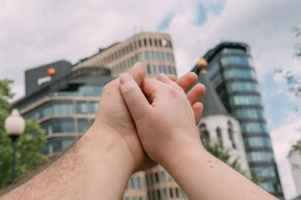 Mãos masculinas e femininas juntas no fundo de uma grande cidade. A mão de uma mulher segura suavemente a mão de um homem contra o fundo de arranha-céus na metrópole - Foto, Imagem