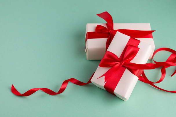 Two white gift boxes tied with bright red bows on an aqua blue background and space for text. Good for Christmas and New Year banners. - 写真・画像