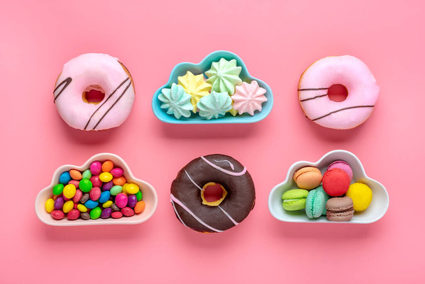 雲の形をしたボウルの中のお菓子とメレンゲ、ピンクの背景に隔離されたカラフルなトッピングとピンクのドーナツを持つチョコレートフラットレイトップ表示ノール健康的でおいしい食べ物の概念. - 写真・画像