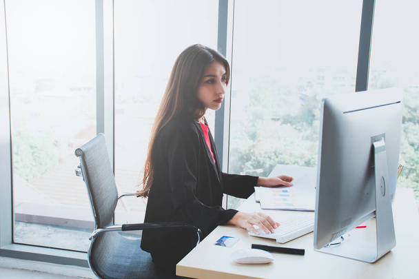Genç bir iş kadını ofiste oturup ciddi ciddi düşünüyor ve beyaz bilgisayar üzerinde çalışıyor.. - Fotoğraf, Görsel