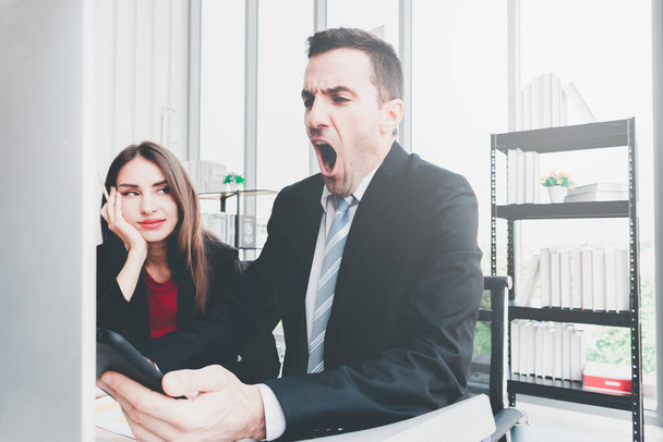 A businessman holding a smartphone yawning while working in the office. The boss is sleepy while working with a beautiful office worker. - Fotoğraf, Görsel