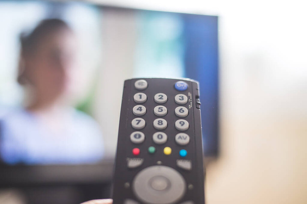 Holding a TV remote control in the hand, foreground, tv in the blurry background. Streaming. - Foto, immagini